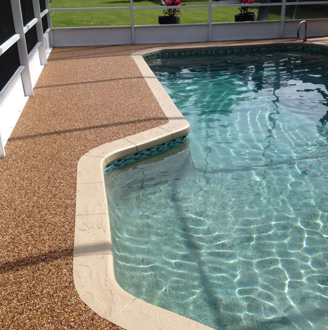 Curved pool edge beside a tan textured deck, with clear blue water shimmering in sunlight