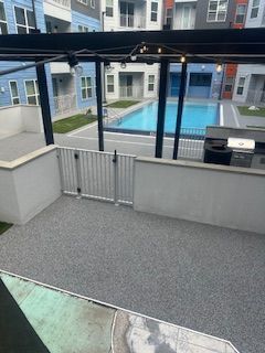 Apartment patio with gray flooring, white railing, and a view of a pool courtyard