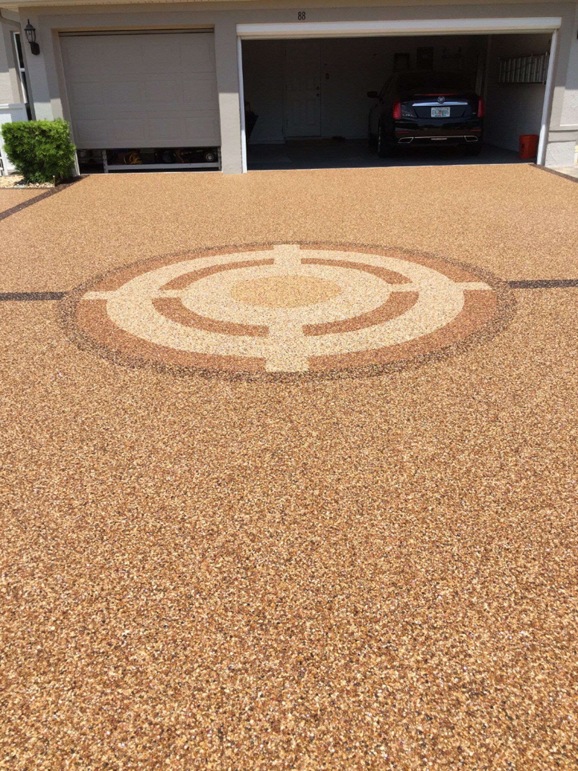 Textured tan driveway with a large circular emblem in front of an open garage with a car inside