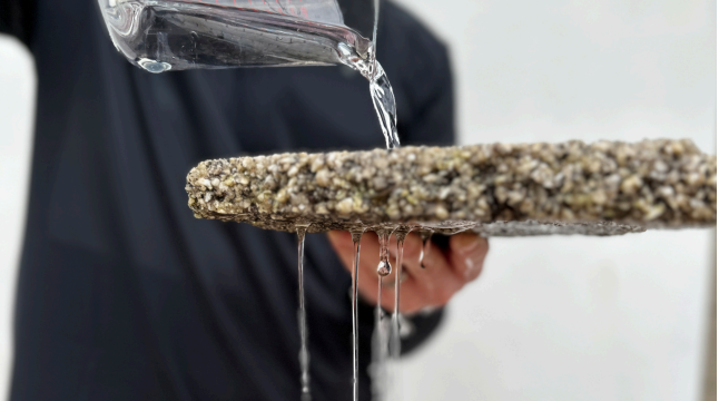 Water pouring from a glass onto a rough stone slab held over a sink