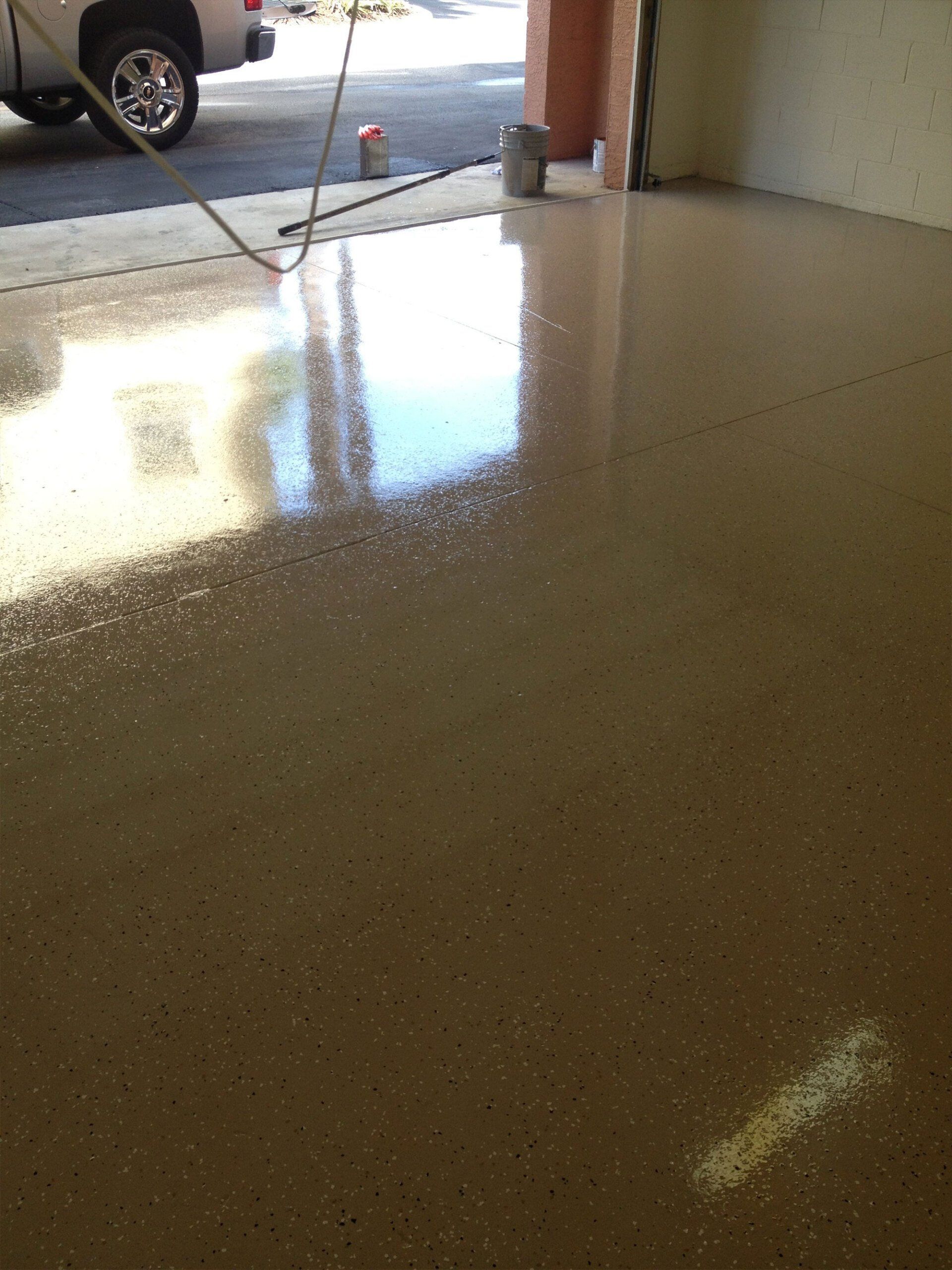 Shiny speckled garage floor with reflections, open to driveway and a parked car outside.