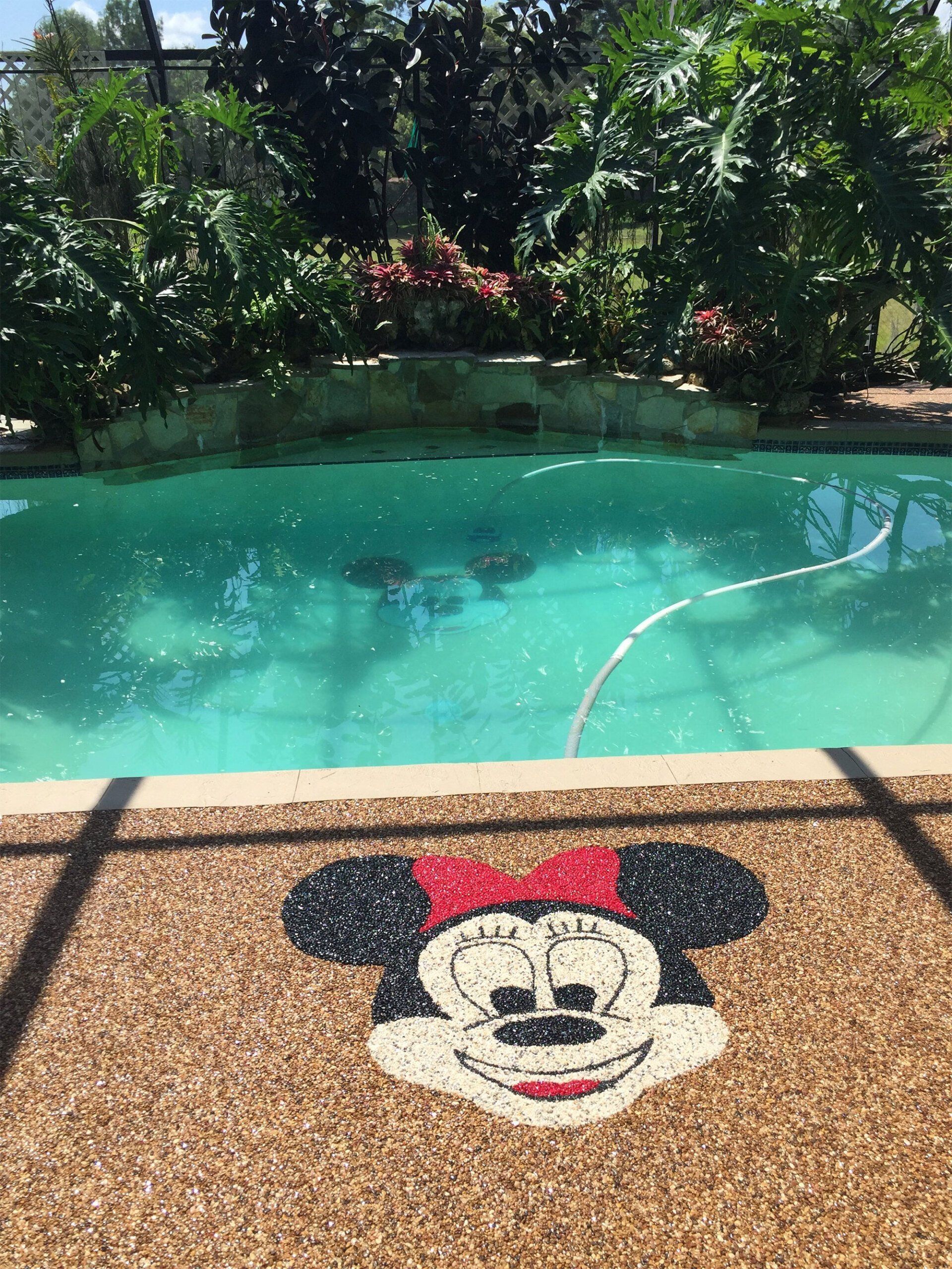 Mickey Mouse face mosaic beside a turquoise swimming pool with lush greenery in the background