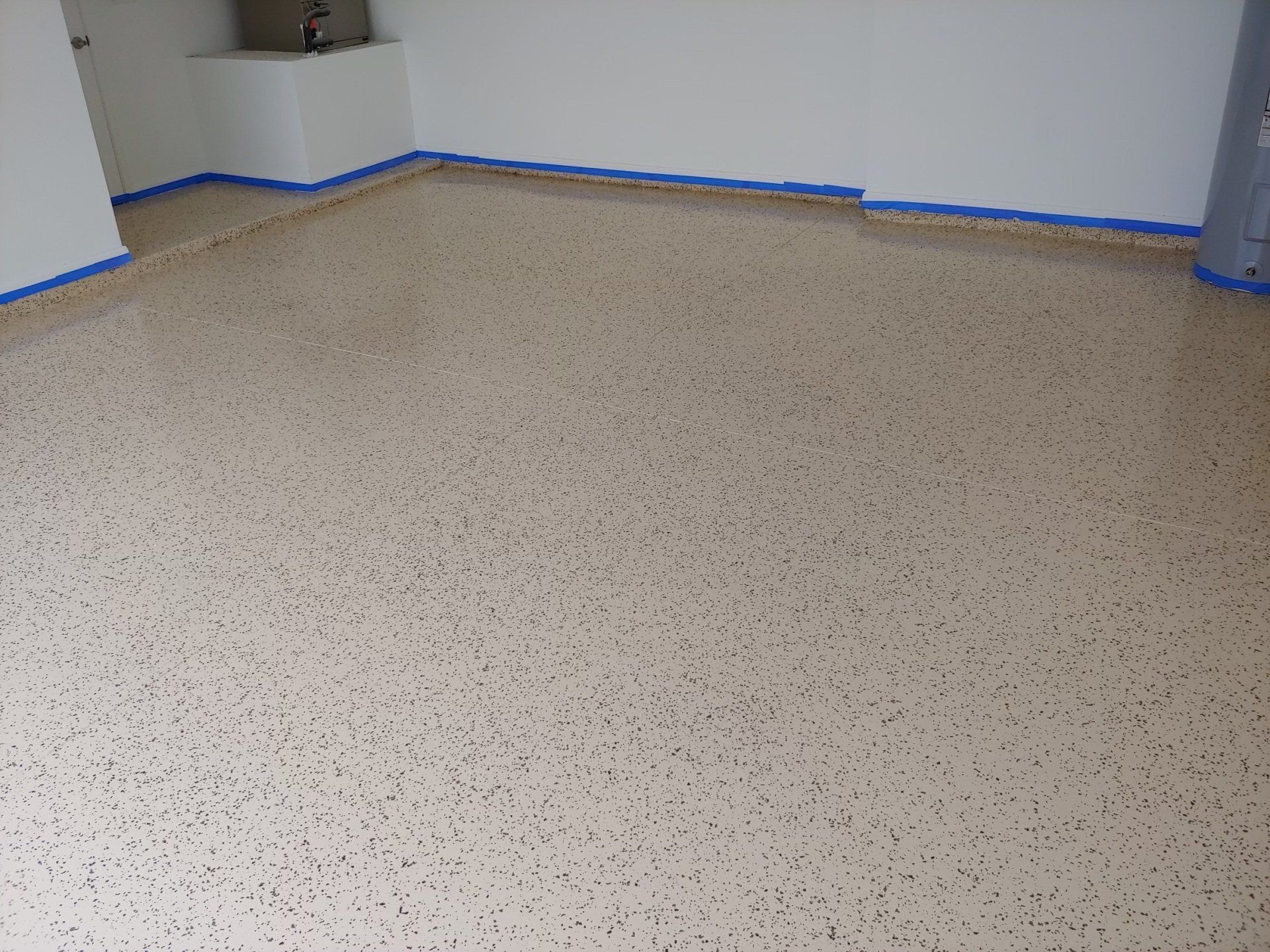 Empty room with speckled floor and white walls, blue painter’s tape along the baseboards