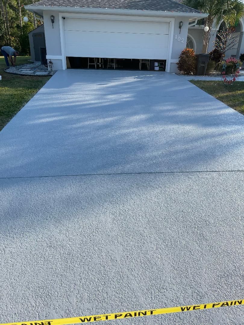 Freshly paved light gray driveway leading to a house garage, with yellow caution tape at the bottom edge.