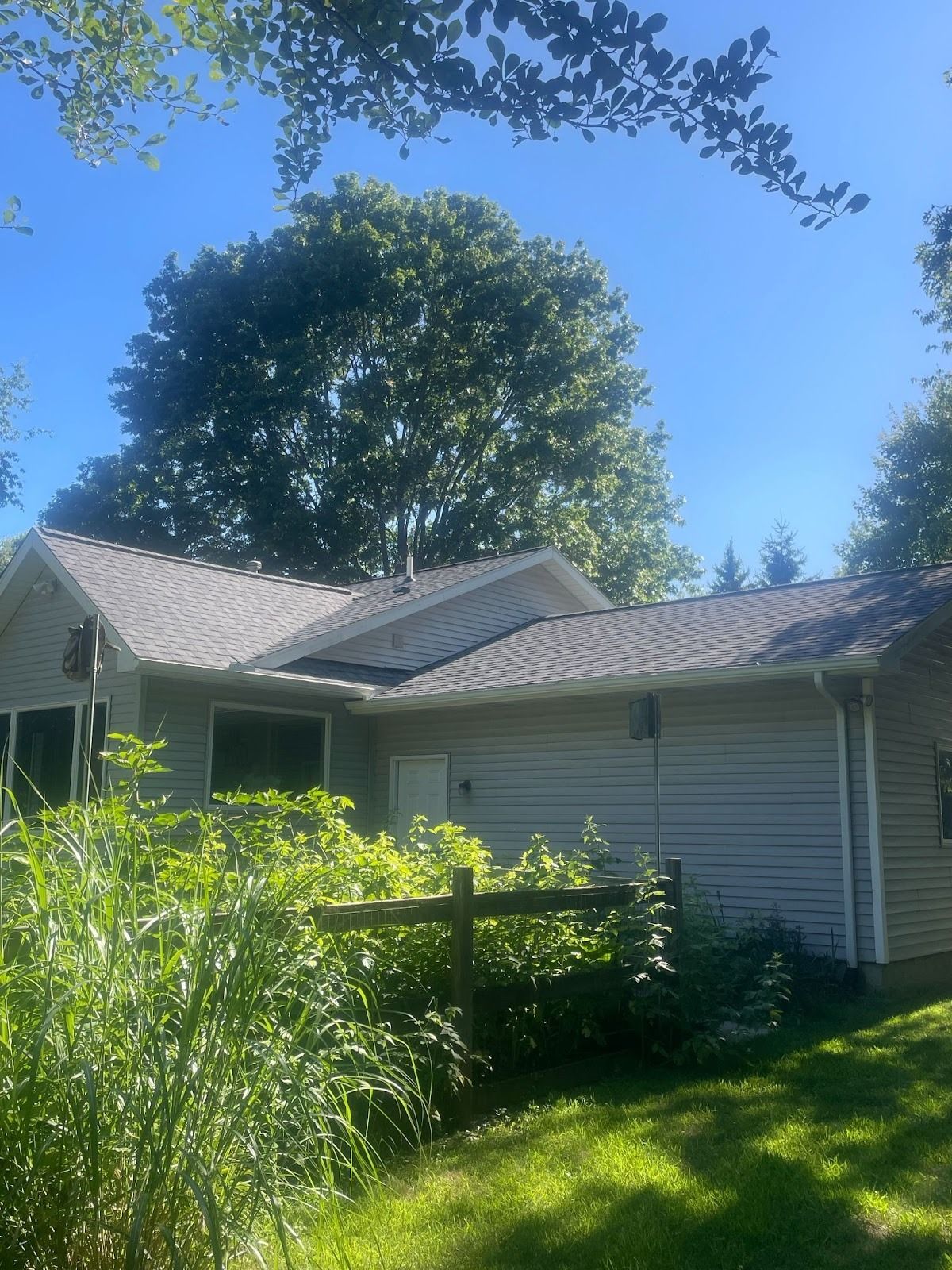 Gray house with gray roof, surrounded by green foliage, under a blue sky.