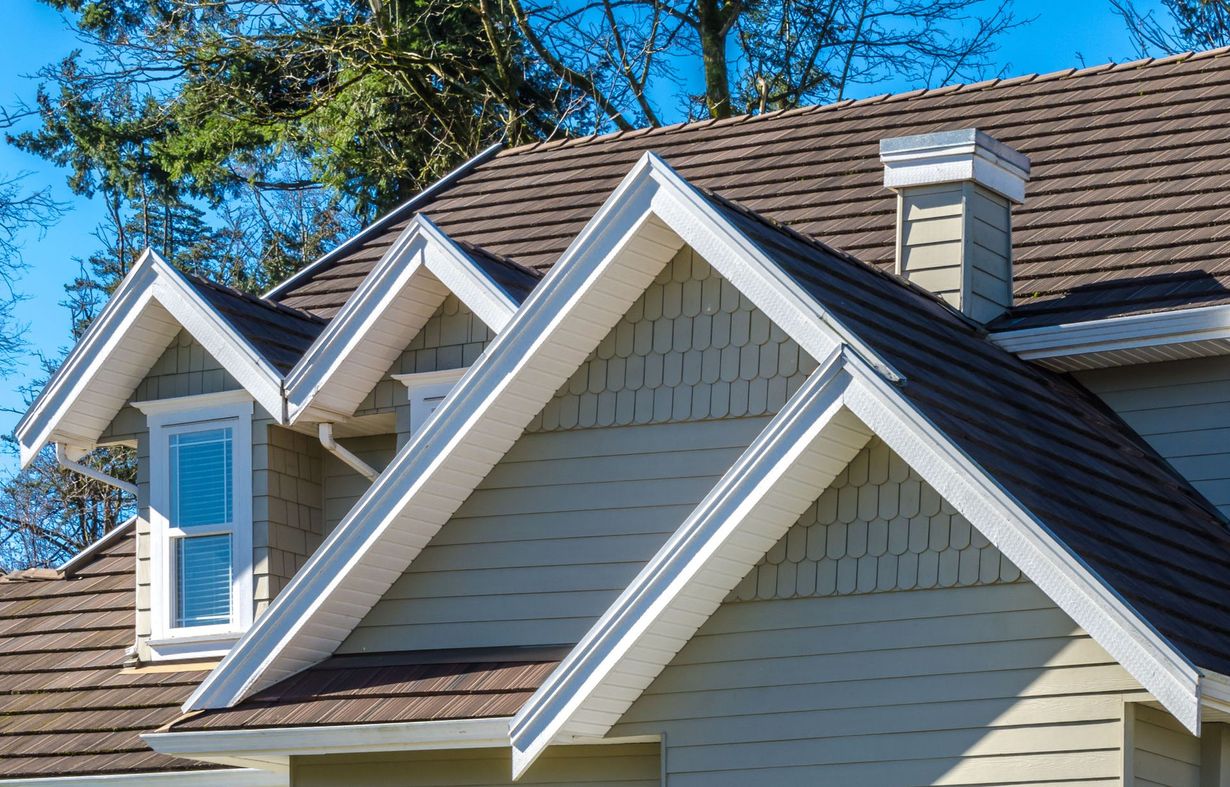 House roof with multiple gables, gray shingles, white trim, and a chimney under a blue sky