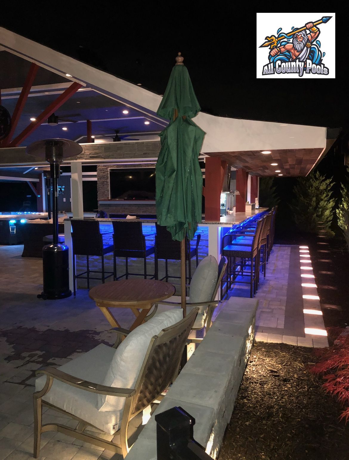 A patio with a green umbrella and chairs at night