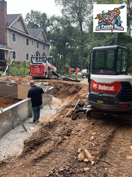 A man is standing next to a bulldozer on a dirt road in front of a house.