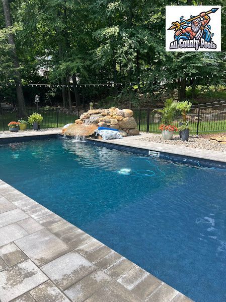 A large swimming pool with a waterfall in the backyard surrounded by trees.