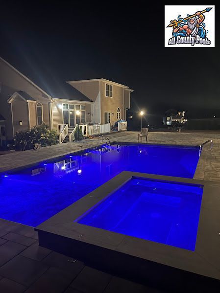 A large swimming pool is lit up at night in front of a house.
