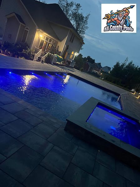 A large swimming pool is lit up at night in front of a house.