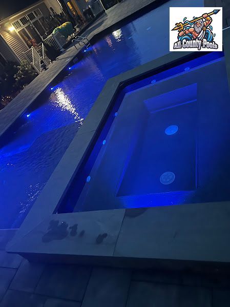 A large swimming pool is lit up at night with blue lights.