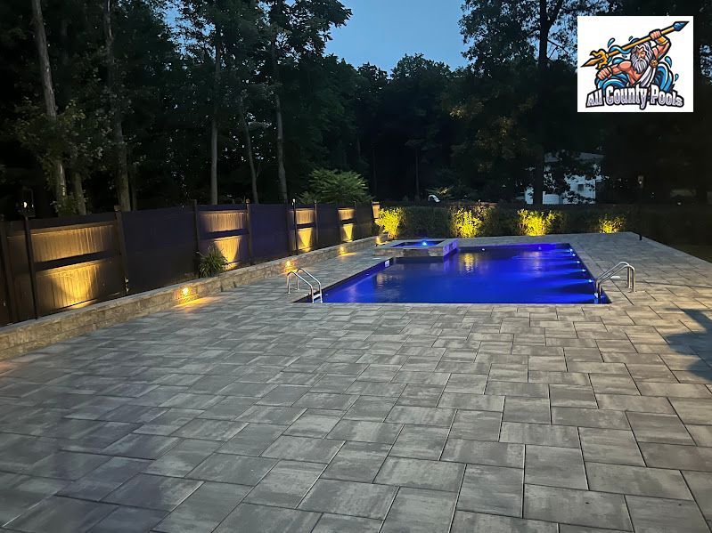 A large swimming pool is lit up at night in a backyard.