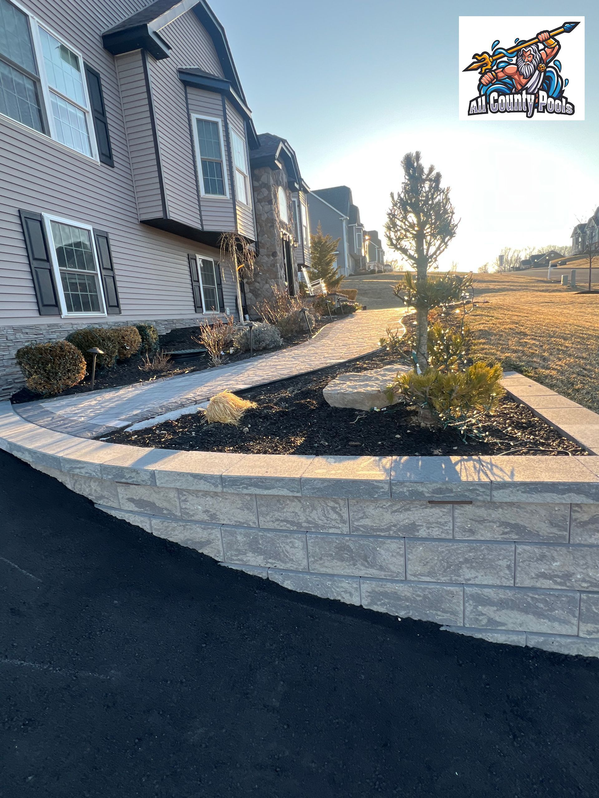 A house with a walkway and a brick wall in front of it.