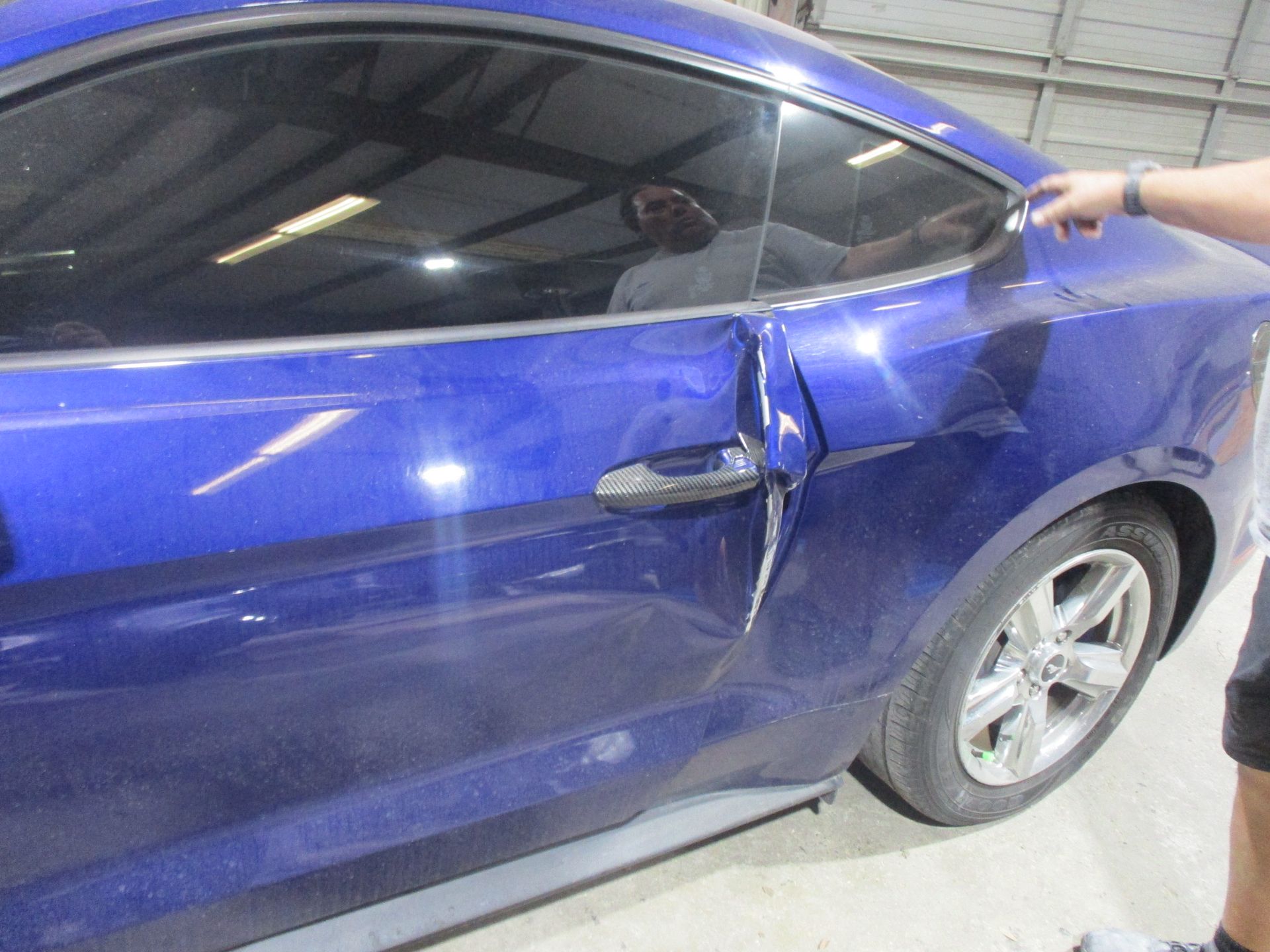 A man is standing next to a blue car with a damaged door.