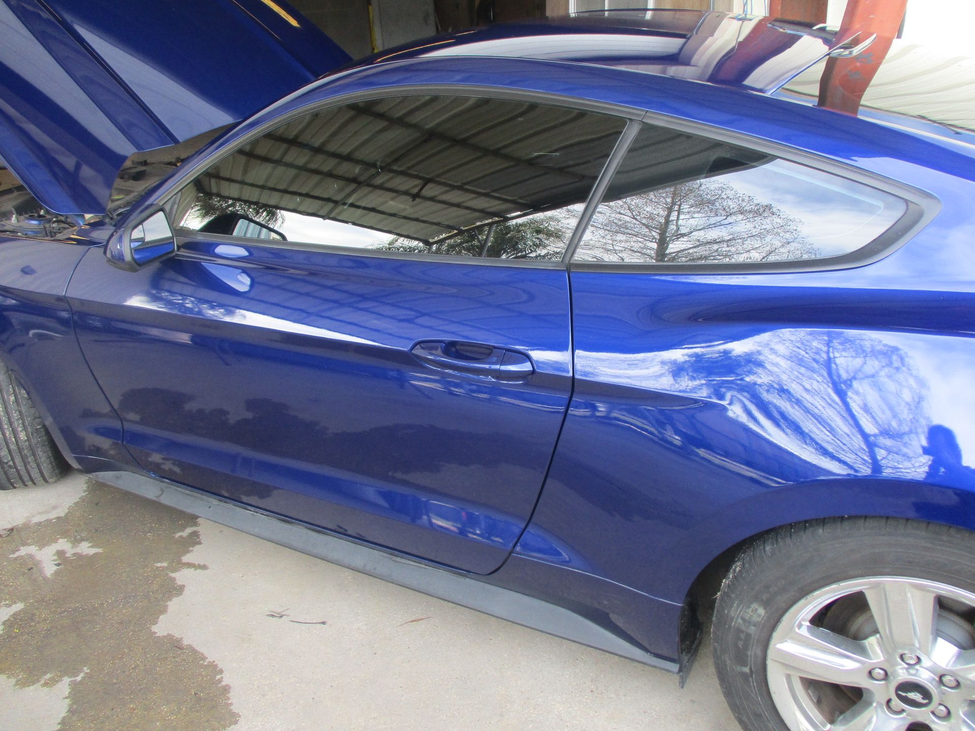A blue car with the hood up is parked in a garage.