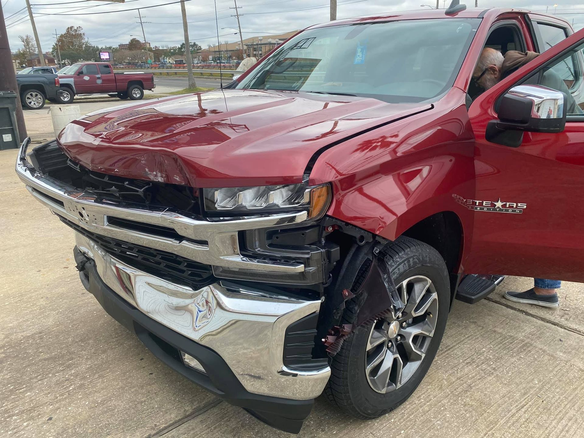 A red truck with a damaged front end is parked on the side of the road.