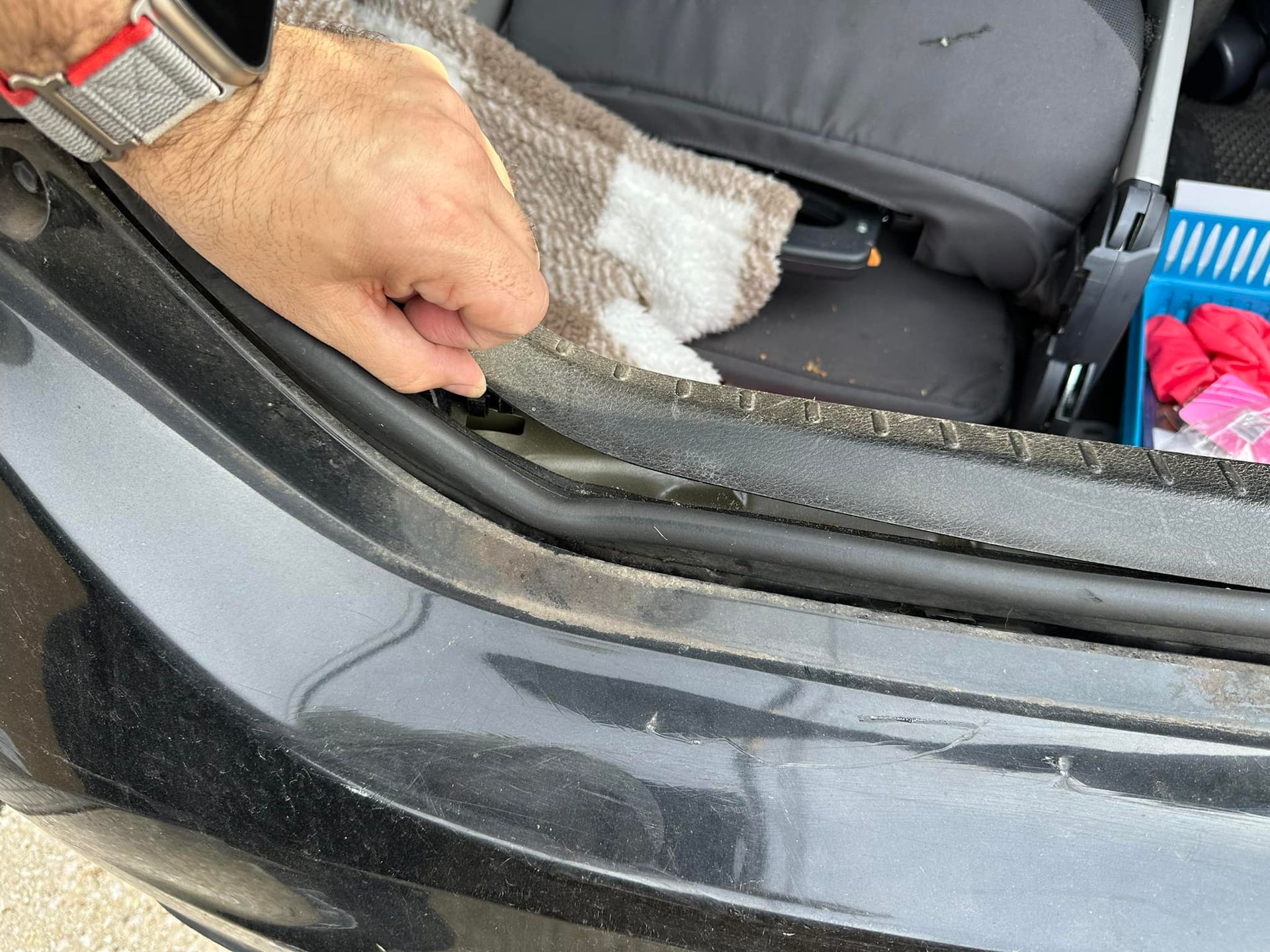 A person is cleaning the back of a car with a towel.