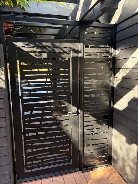 Black metal gate with horizontal cutouts, wooden deck and siding.