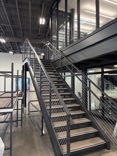 Staircase with metal railings and wooden steps leading to a mezzanine level in a modern building.