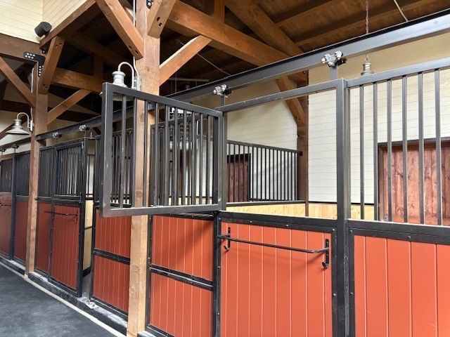 Horse stable interior with red doors, black iron bars, and wooden beams.