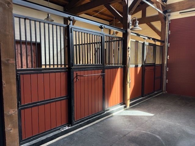 Horse stalls with red and tan wood panels and black metal bars.