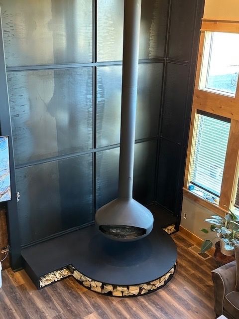 Modern black fireplace with a suspended, spherical firebox and tall chimney against a dark wall.