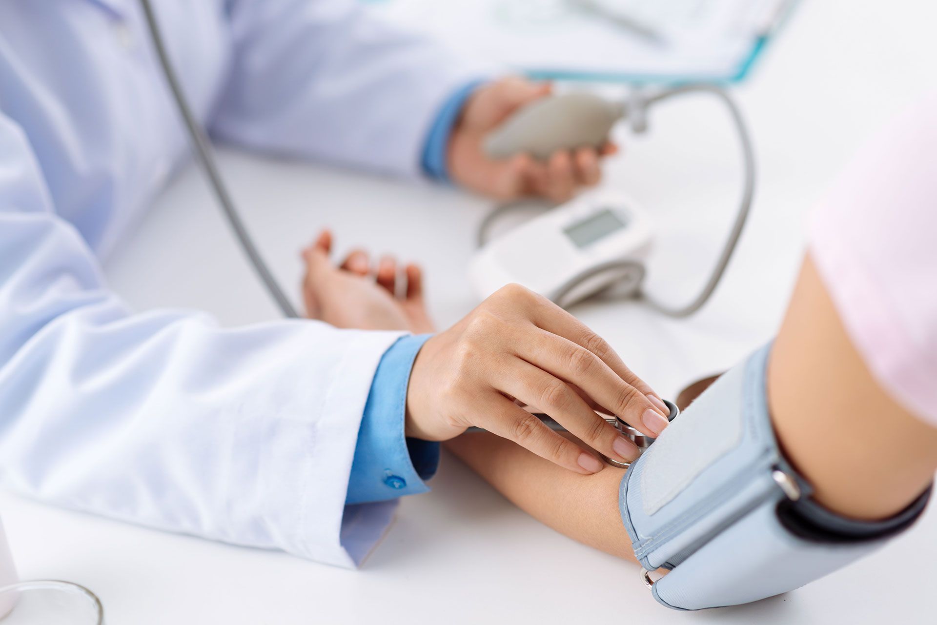Doctor taking a patient's blood pressure with a digital monitor in a clinical setting.