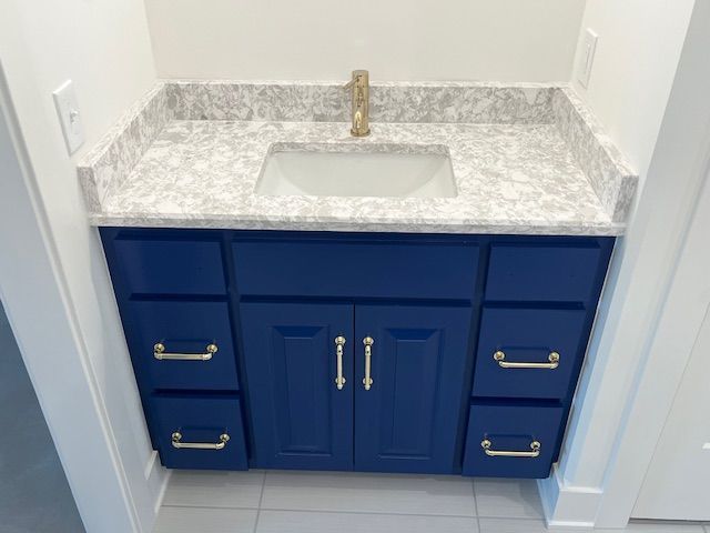 A bathroom vanity with blue cabinets and drawers and a sink.