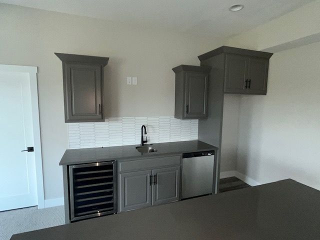 A kitchen with gray cabinets , a sink , a refrigerator and a wine cooler.