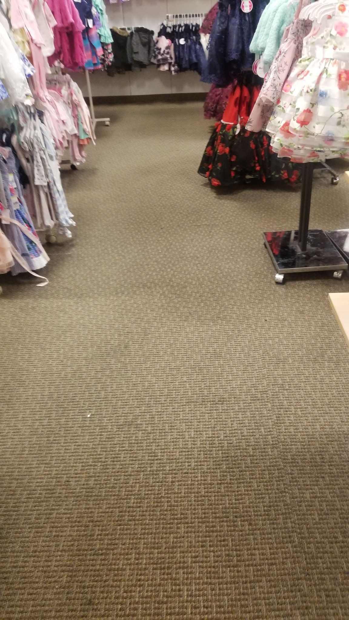 Clothing store aisle with dresses and a patterned carpet.