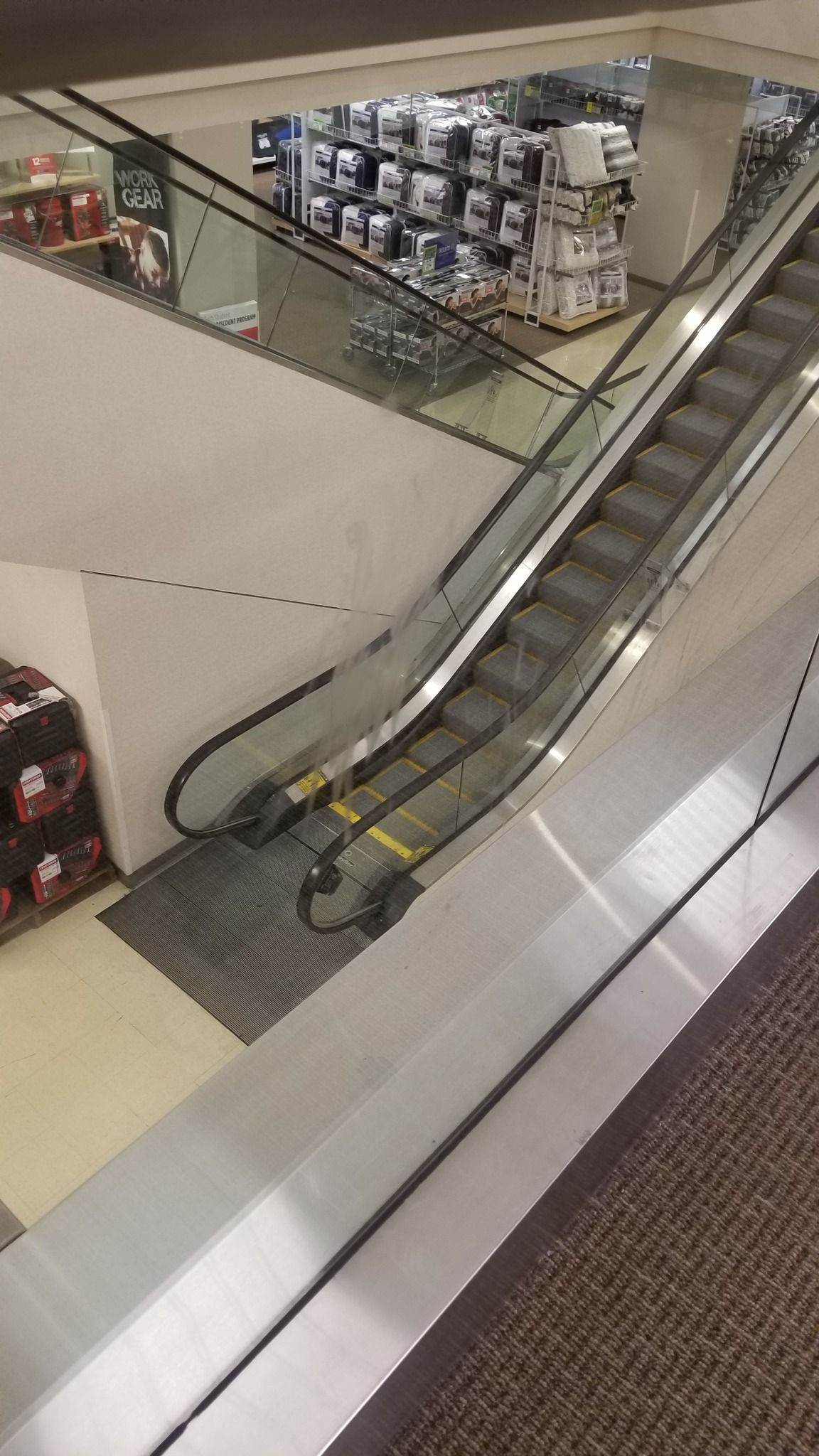Escalator in a store with paint cans stacked in the background.