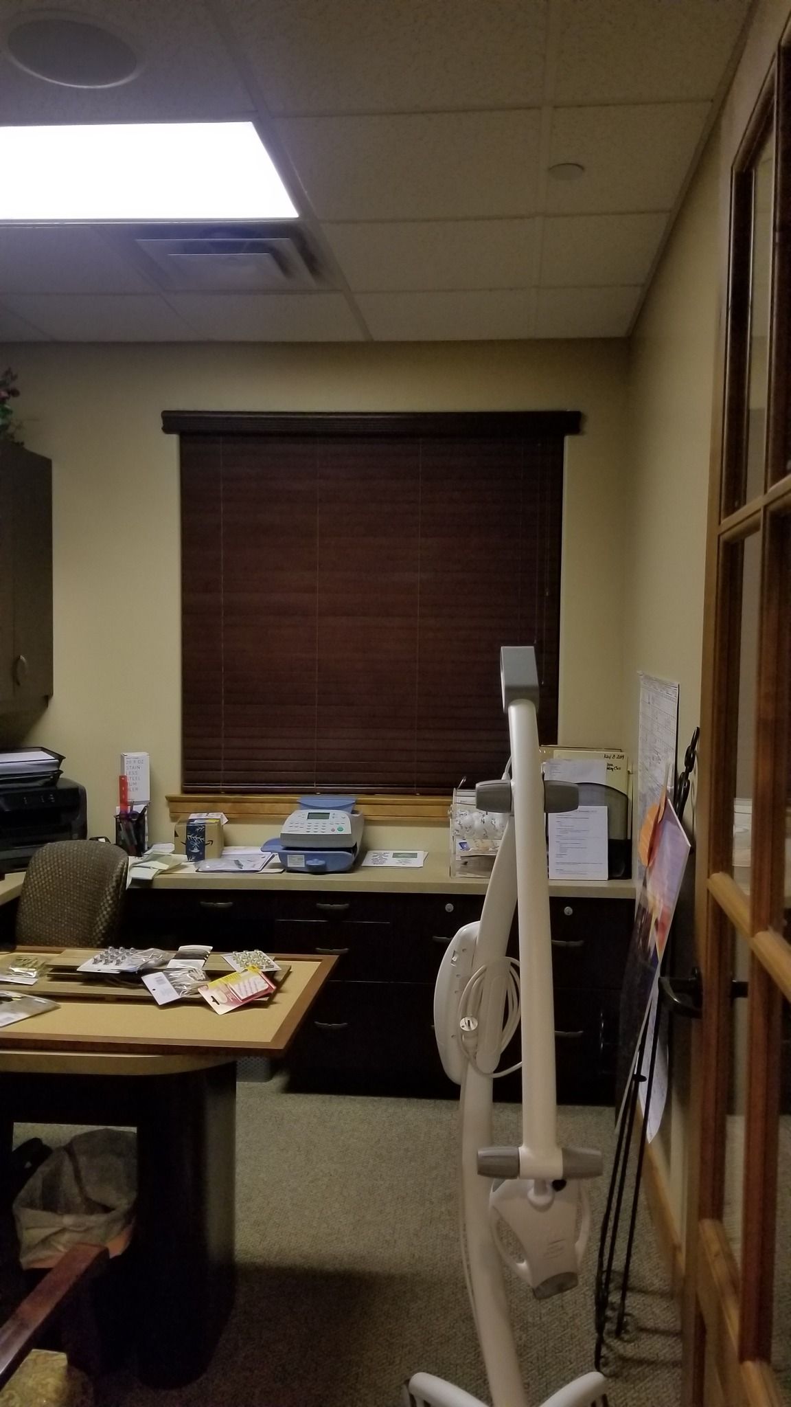 Office with dark brown blinds, desk with printer and papers, and medical equipment.