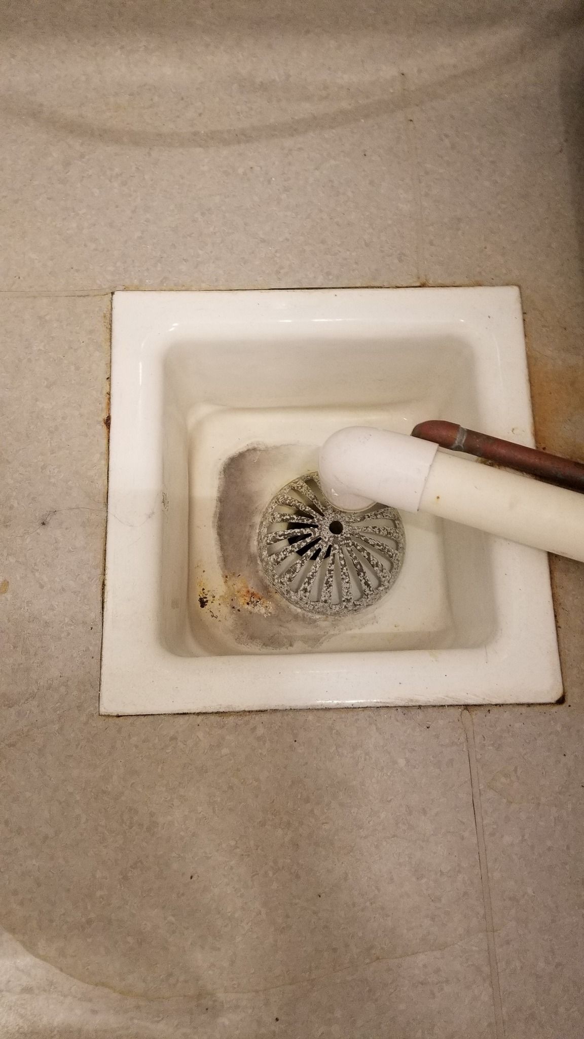 White drain basin with metal strainer being cleaned by a person using a white pipe and copper pipe.