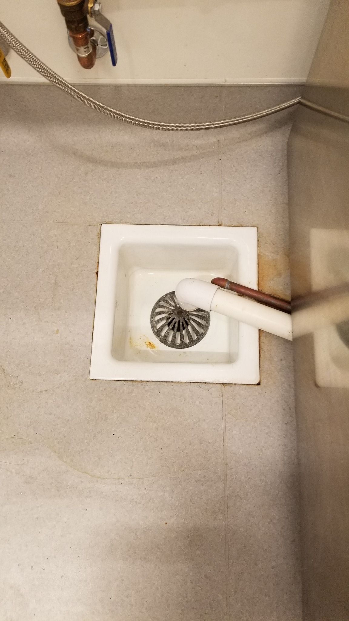White drain in a gray floor, with a white pipe inserted into it, and plumbing visible above.