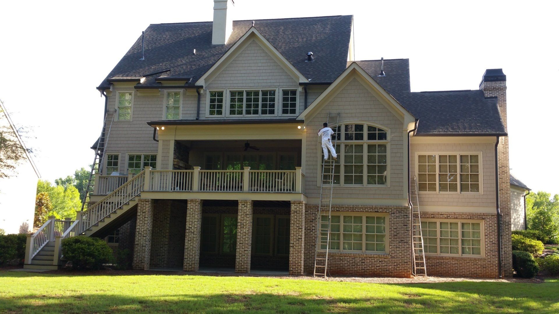 A large house is being painted by a man on a ladder.