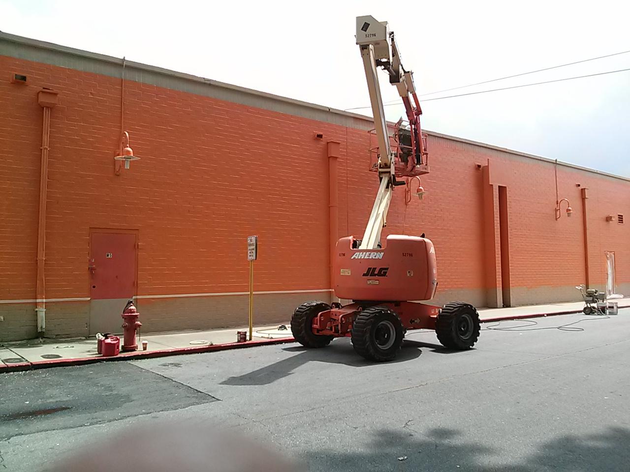 A red jlg lift is parked in front of a large orange building.