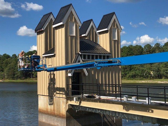 A man on a lift is working on a building next to a body of water.