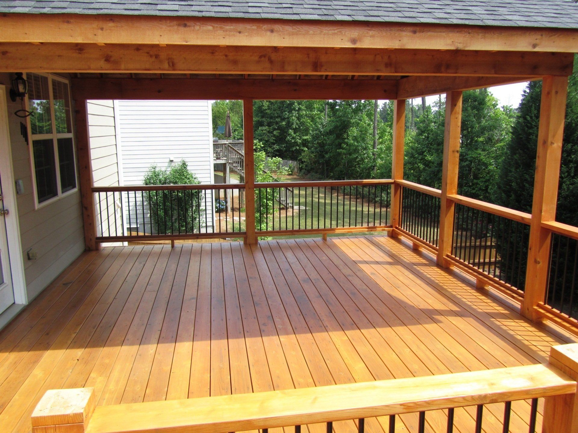 A large wooden deck with a railing and a house in the background