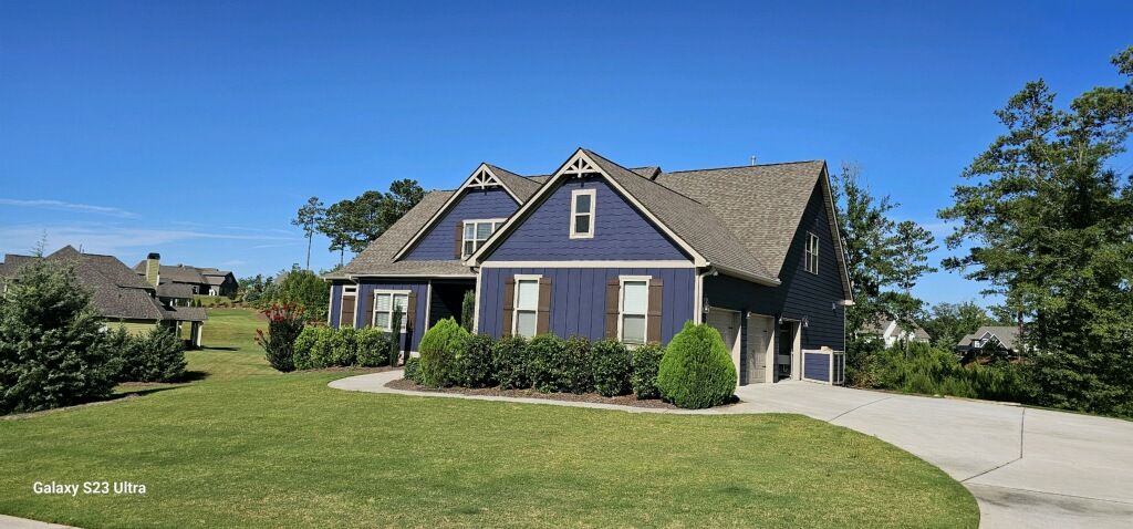 A blue house with a gray roof is sitting on top of a lush green field.