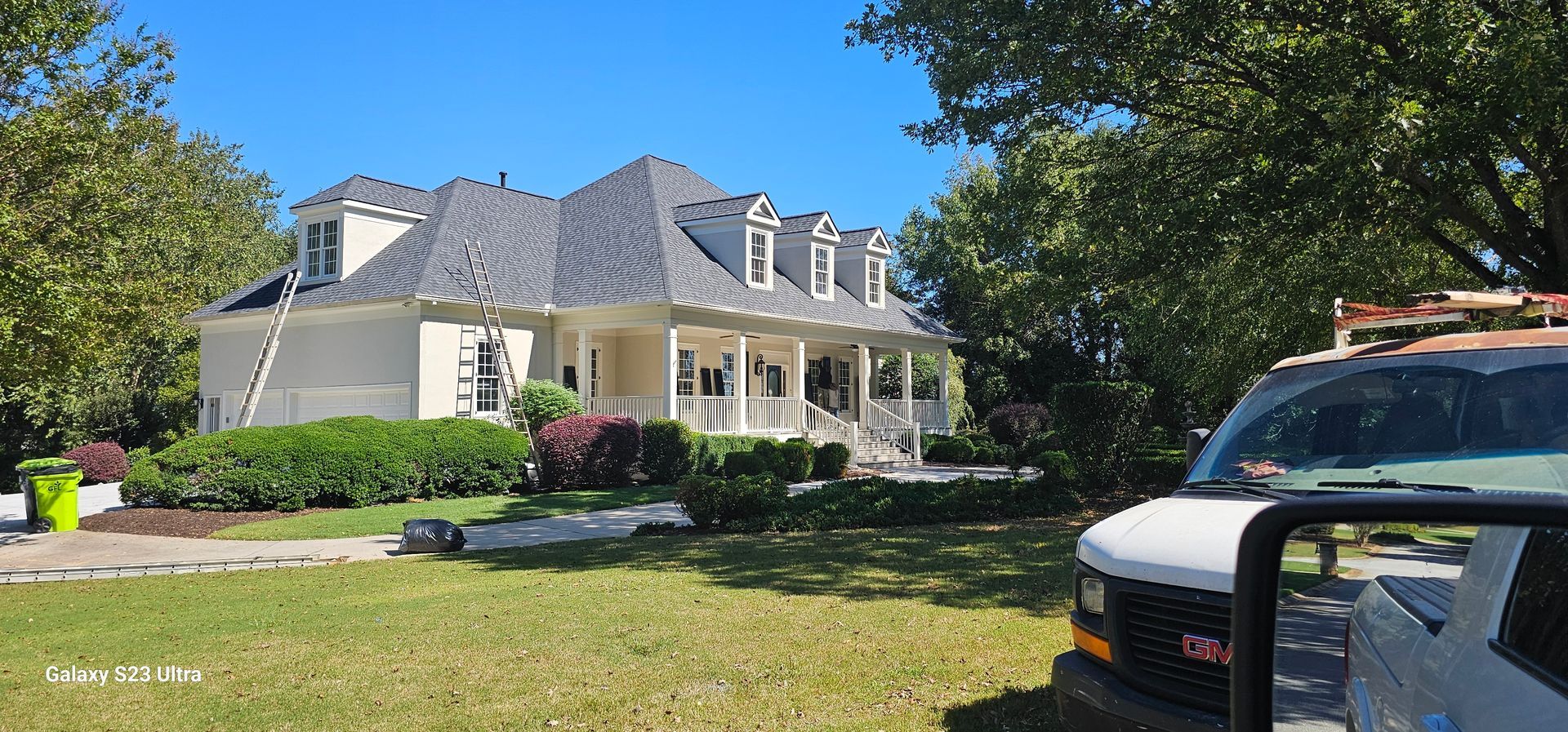 A white van is parked in front of a large white house.