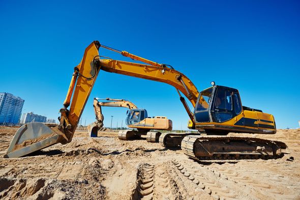 Two yellow construction excavators on a dirt lot under a clear blue sky.