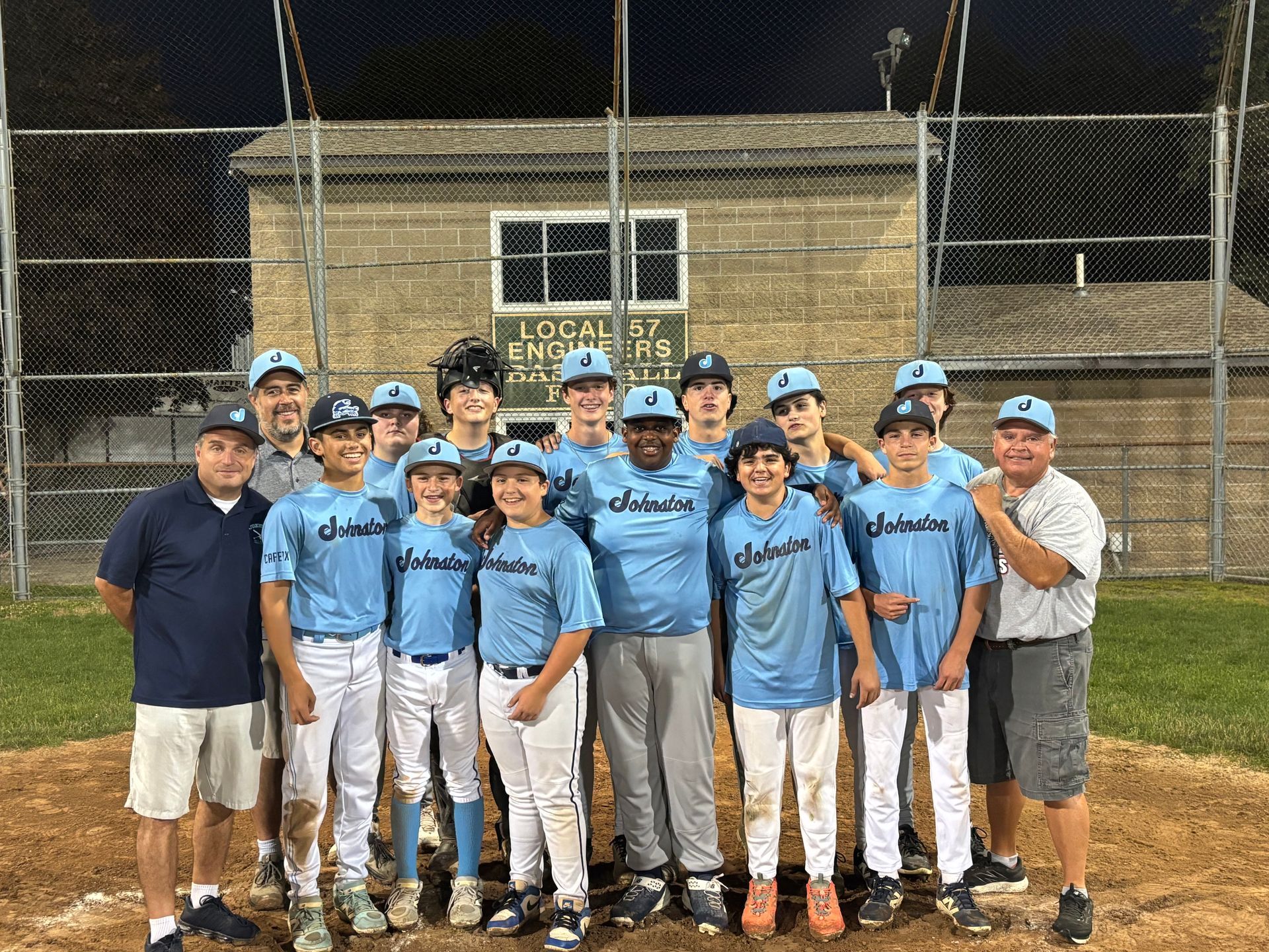 Youth baseball team and coaches posing on a field at night, wearing light blue jerseys and white pants