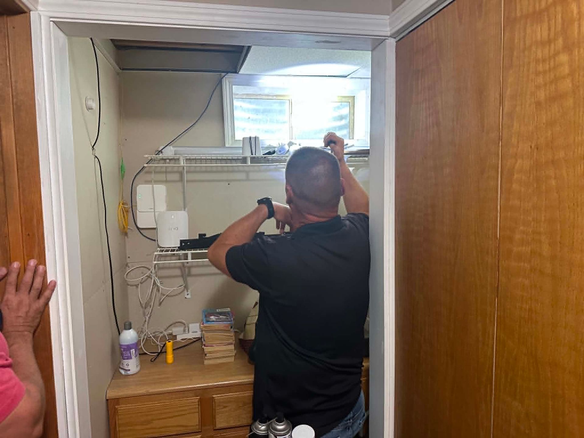 Person inspecting for bug control in a small utility closet by a bright window.