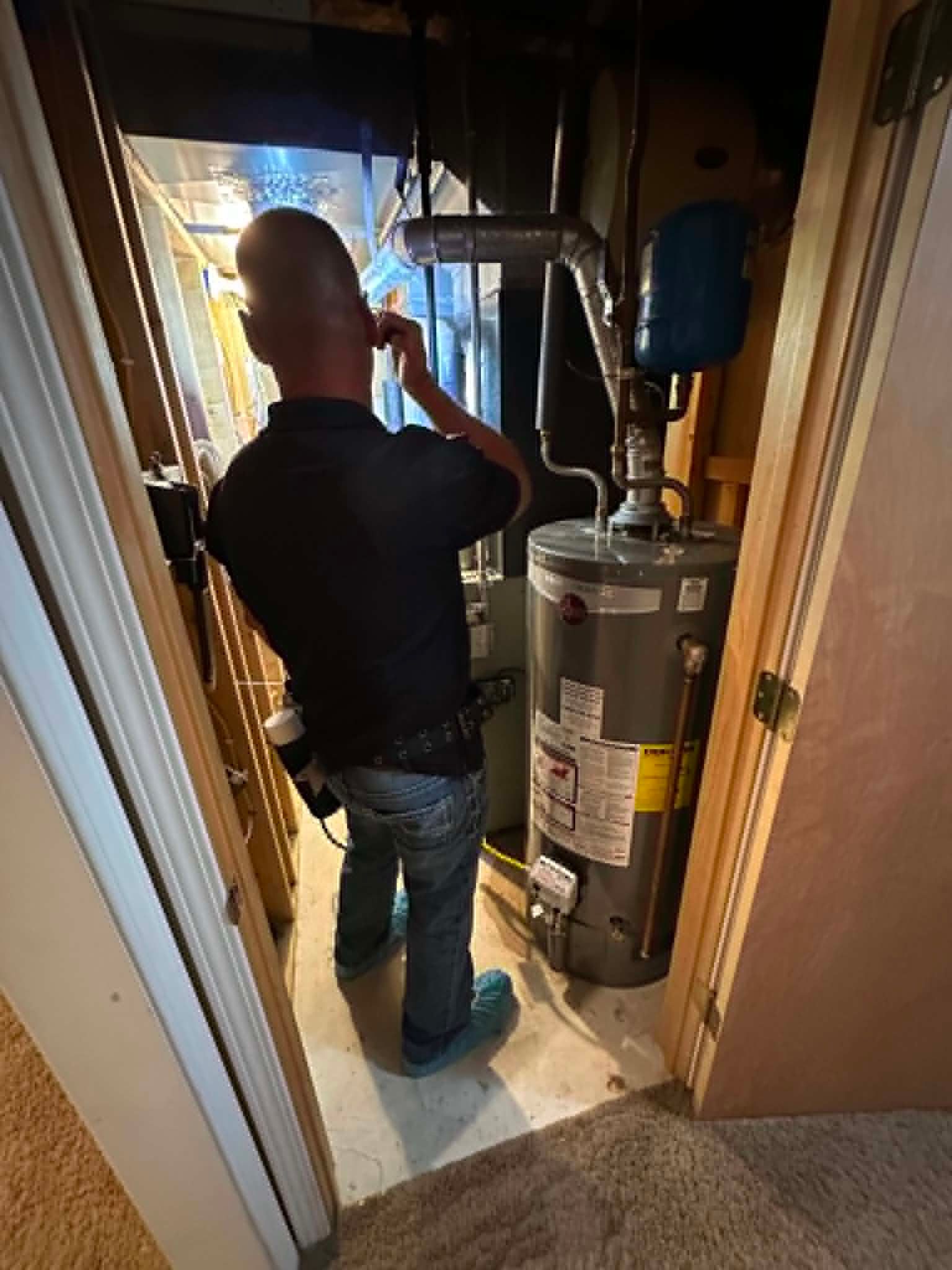 Person standing in a narrow utility closet beside a water heater and furnace, inspecting for bug control.