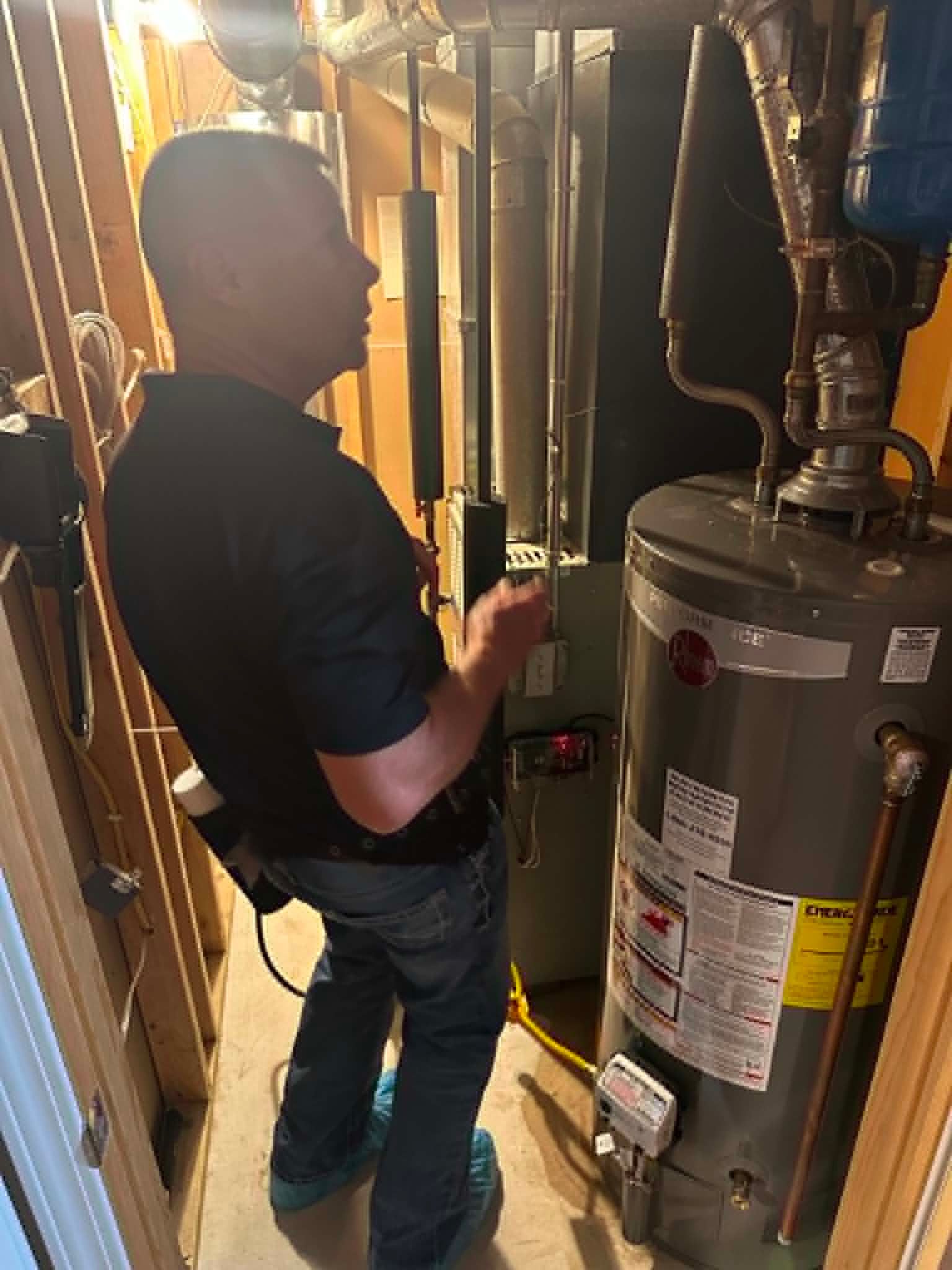 Technician inspecting a water heater in a basement utility room for bug control.