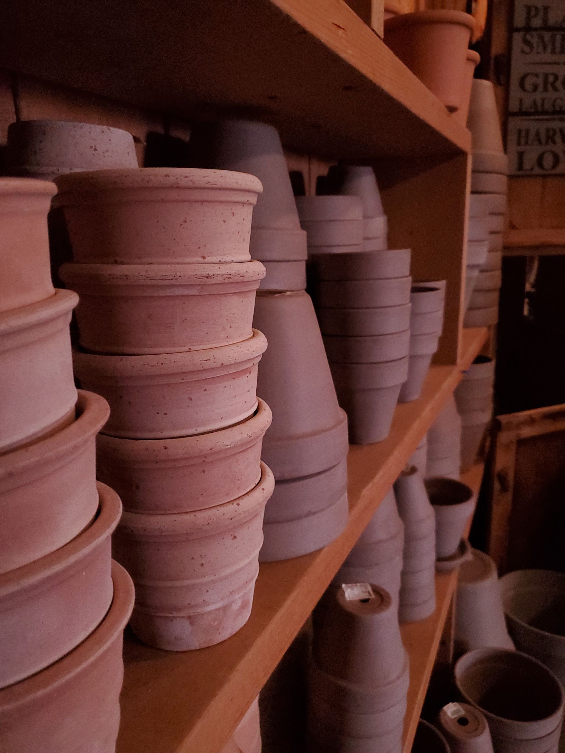 Many pots are stacked on a wooden shelf with a sign in the background that says pottery