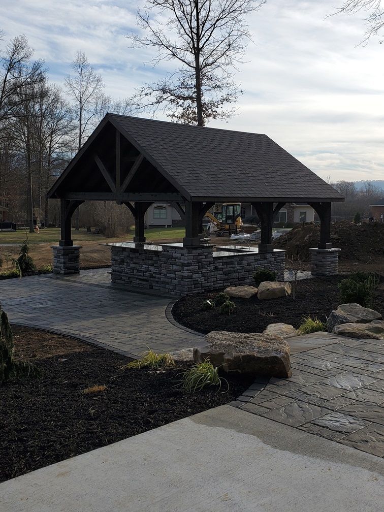 A gazebo in the middle of a garden with a concrete walkway leading to it.