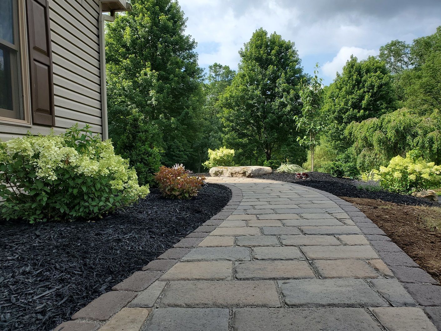 A brick walkway leading to a house surrounded by trees and bushes.