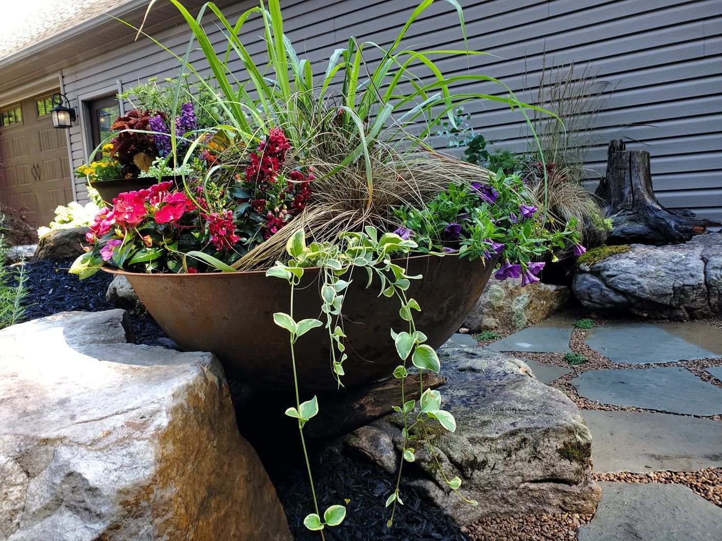 A large bowl filled with flowers is sitting on a rock in front of a house.